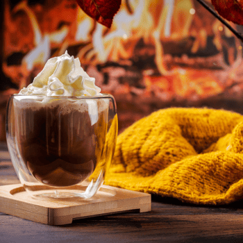 A glass of hot chocolate by a fire.