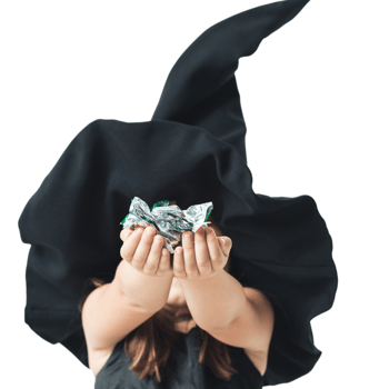 Little girl in a witch hat holding candy out