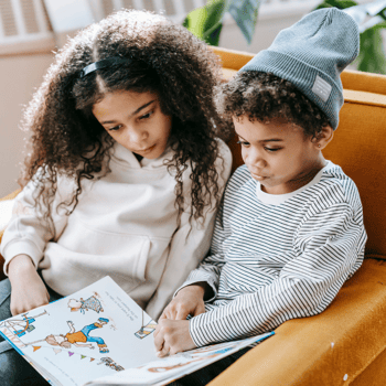 A little boy and girl reading a book together in a big orange chair.