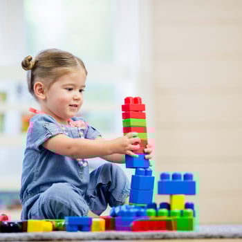 A little girl building a lego tower.