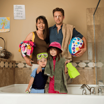 A family in their bathtub with summer gear like a beach ball, goggles, and flippers.