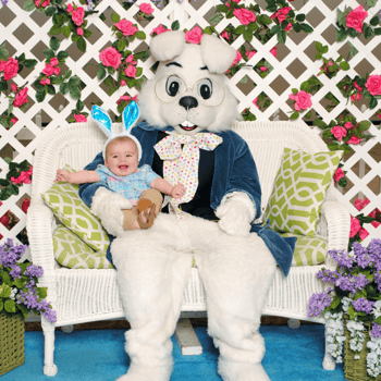 A baby with blue bunny ears on giggling with the easter bunny.