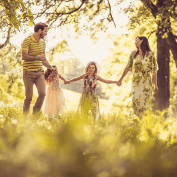 A family holding hands and walking through a field in warm spring sunlight.