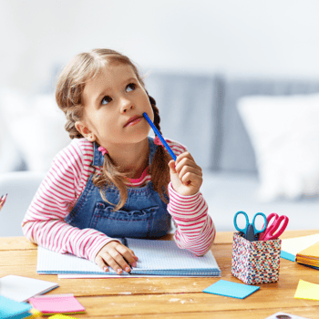 A little girl thinking with her pen next to her mouth while doing homework.
