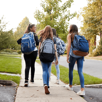 Group of teens walking on sidewalk with backpacks.