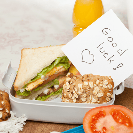 A sandwich in a lunch box with a note that says "good luck!"