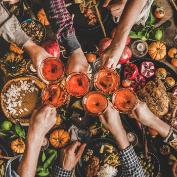 Friends cheersing their drinks over a friendsgiving meal.