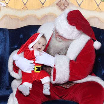 Baby with an oversized Santa hat giggling with Santa.