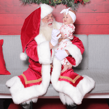 Baby girl laughing holding Santa's hand.