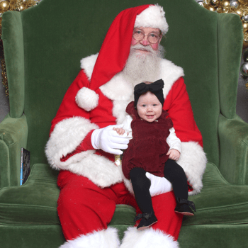 Baby girl in a red dress and bow smiling with Santa.