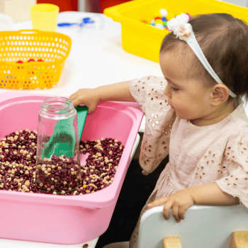 A little girl playing with dried beans in a sensory bin.