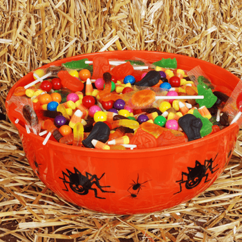 Candy in a halloween bowl sitting on bales of hay.
