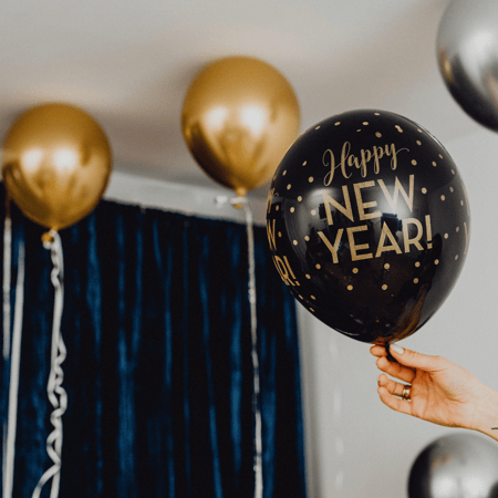 A black balloon that says Happy New Year in gold with gold polkadots.