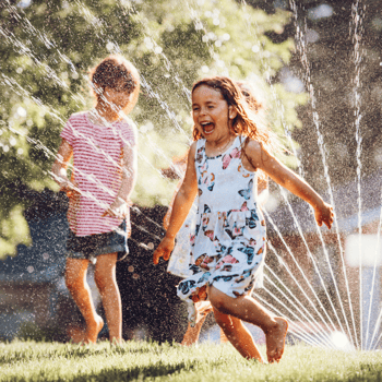 Two kids running through a sprinkler.