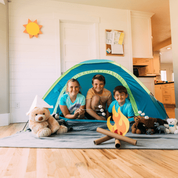 Kids in a camping tent inside with a fake fire roasting marshmallows.