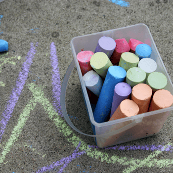 Side walk chalk in a plastic bin with scribbles on the ground.