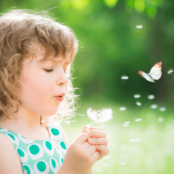 A girl blowing a dandelion with a butterfly flying by.