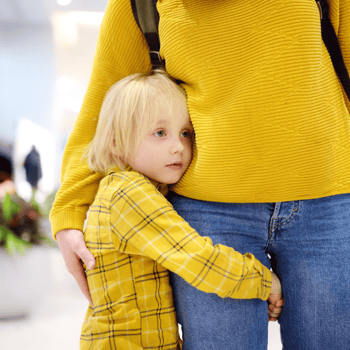 A little girl hugging her moms leg.