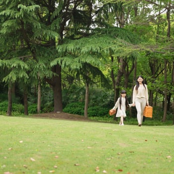 A little girl and her mom walking in a field for a Picnic.