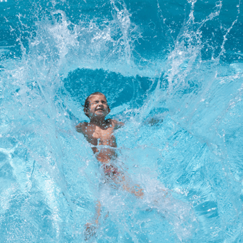 A little boy making a big splash in a pool.