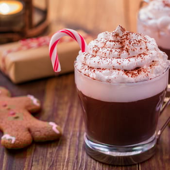 A glass of hot chocolate with whipped cream and a candy cane.