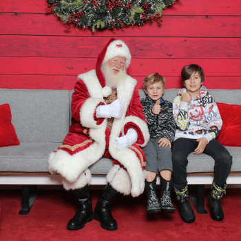 Two brothers sitting with Santa giving a thumbs up.