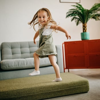 Little girl jumping on couch cushions.