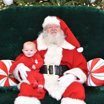 A baby sitting with Santa smiling.