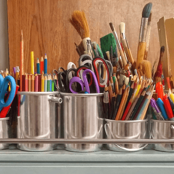 A shelf full of art supplies like scissors, colored pencils, and paint brushes.
