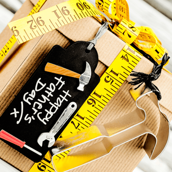 A box with a hammer cookie cutter and measuring tape ribbon with a tag that says happy fathers day.