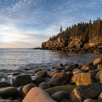 A rocky beach next to a mountain in the sunset.