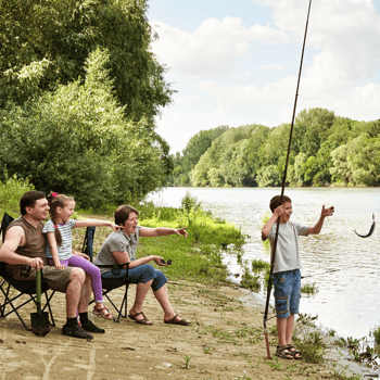Kids fishing with their parents on the edge of a lake.