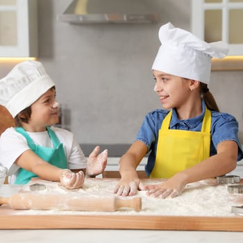 Kids baking with flour in the kitchen with chefs hats.