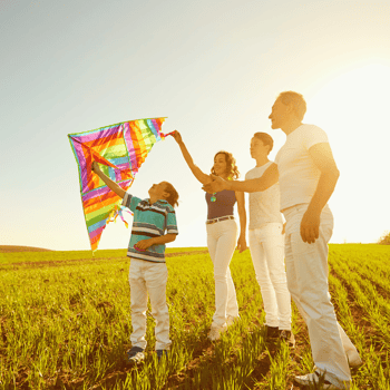 A family flying a colorful kite on a hill on a sunny Spring day.