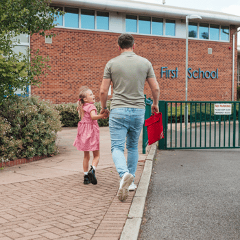 A dad and daughter walking together into the school building.