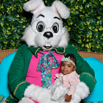A baby girl in a cute floral dress sitting with the Easter bunny.