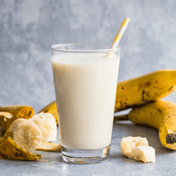 Banana smoothie in a glass surrounded by bananas.