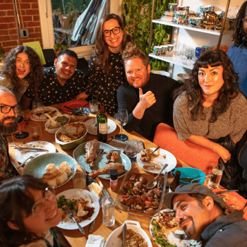 A group of friends smiling at the camera after a friendsgiving meal.
