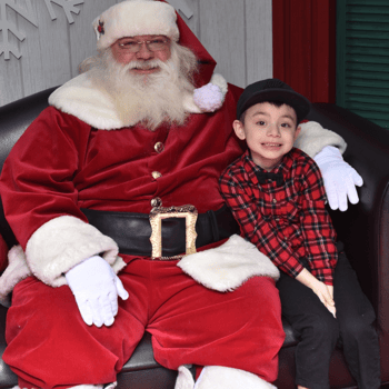 A little boy in a red plaid shirt and black hat smiling with Santa.