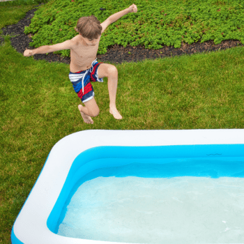 A little boy jumping into an inflatable pool.