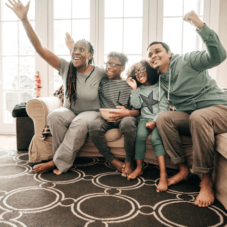 A family sitting on the couch with popcorn watching a movie acting excited about a scene.
