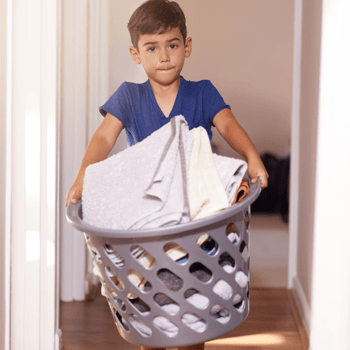 A little boy carrying a basket of folded laundry.