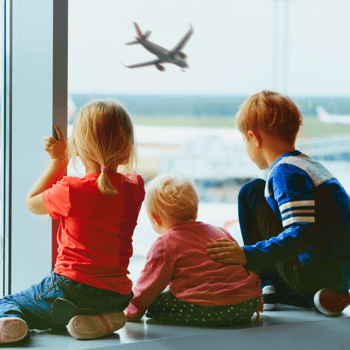 3 little kids looking out the window at an airport.