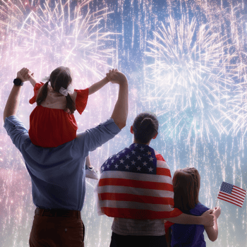 A family watching fireworks together holding American Flags.