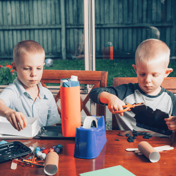 Two boys doing crafts with recycled materials.