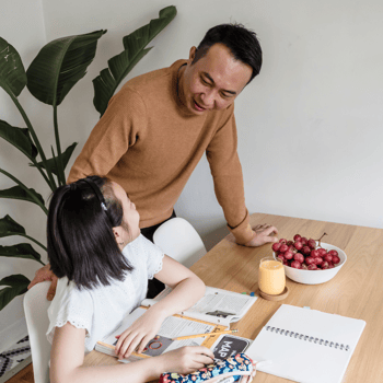 A dad checking in on his daughter doing homework with a snack near by.
