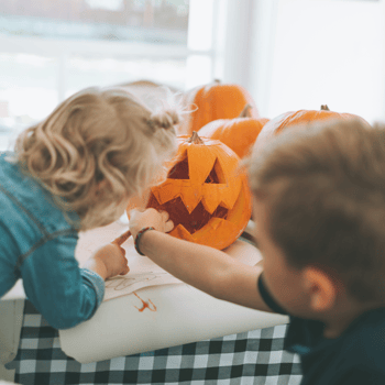 Two kids carving a pumpkin together.