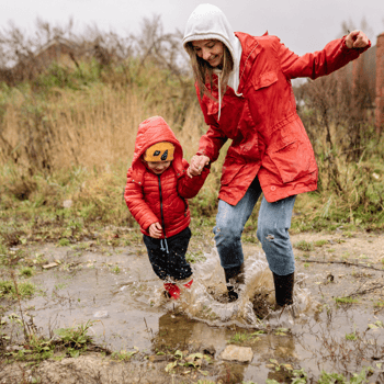 A toddler playing in a puddle with their mom.