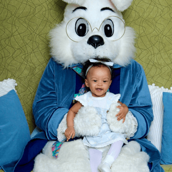 A little girl in a blue dress sitting with the Easter bunny.