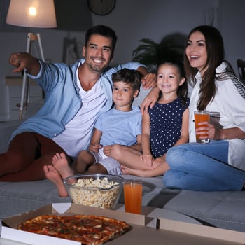 A family watching a movie together with pizza and popcorn.